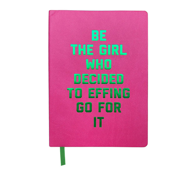 A white background with a pink journal in front of it. The journal is pink with green, metallic lettering. The lettering says "Be the Girl Who Decided to Effing Go For It." 