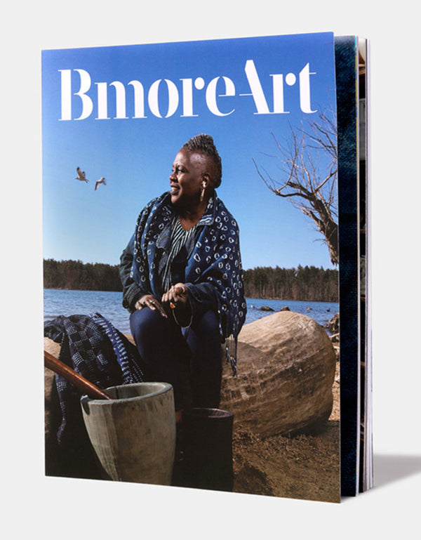 A magazine cover featuring a photograph of a woman with a dark skin tone sitting on a tree trunk by a lake. The title reads "Bmore Art."