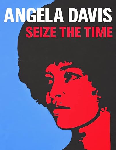 A blue book. Filling the right side of the cover is a pop art style picture of Angela Davis. Her skin in bright red and her hair in black. The title "Angela Davis" is written in white. The subtitle, "Seize The Time" is written in red. 