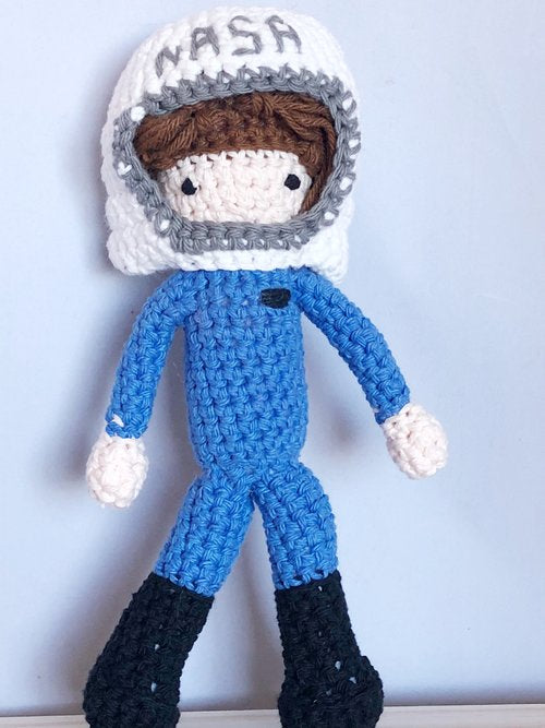 A crochet doll of a person in a blue suit in a white hat that reads "NASA."