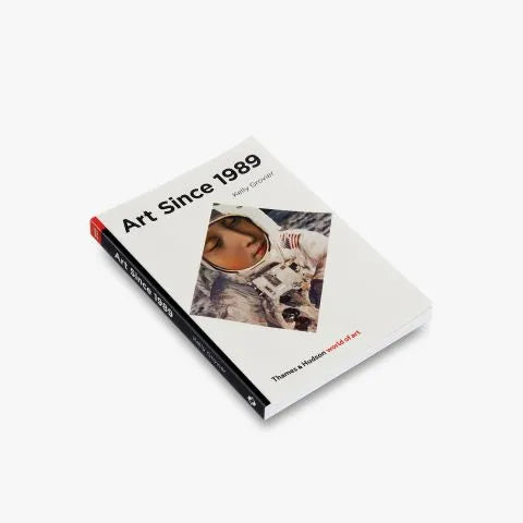 A white background. In the foreground is a white book with a black spine that reads "Art Since 1989." The book has a white cover with a picture that is tilted diagonally in the center of the book. The image features an astronaut on the moon with a painting of a woman's face depicted in the helmet. The title, "Art Since 1989" is written in bold, black letters at the top of the book.  