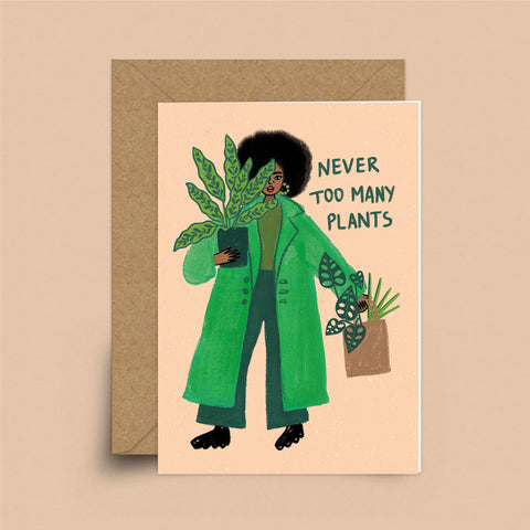 A coral greeting card with a brown envelope. A black woman with natural hair in a green trench coat is holding a potted plant. In her other hand is a basket of plants. Behind her are the words "Never Too Many Plants"