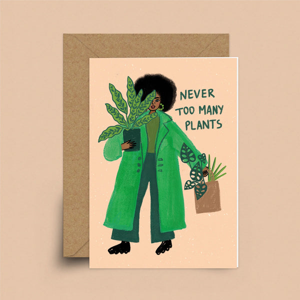 A coral greeting card with a brown envelope. A black woman with natural hair in a green trench coat is holding a potted plant. In her other hand is a basket of plants. Behind her are the words "Never Too Many Plants"