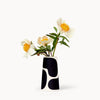 A vase in white with a black color block pattern, resembling mid-century design. Several yellow flowers are standing in the vessel.