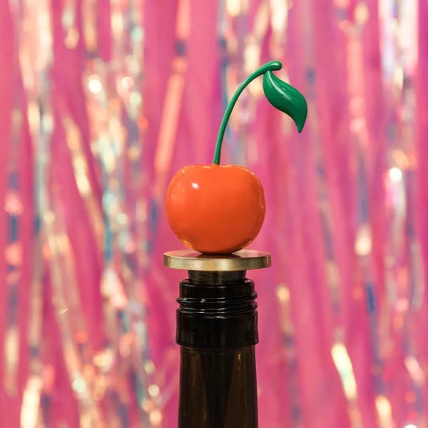 A wine stopper designed in the shape of a cherry sitting on top of a brown bottle.