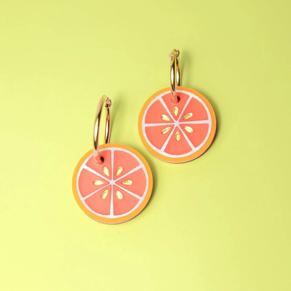 A set of earrings in the shape of orange slices attached to golden hoops.