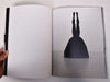 Look inside a book featuring a photograph of a black sculpture upside down. with her legs up in the air.