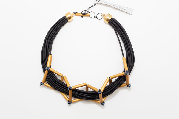 A black and gold necklace made from cords and golden brushed aluminum parts creating geometric shapes around the necklace.