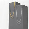 Two dainty layering necklaces in silver and gold hanging in gray pedestals. They are made up of two intertwined sterling chains; one linked and one smooth. 