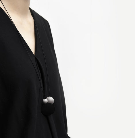 Long necklace with a statement pendant in the shape of three orbs in black and silver.