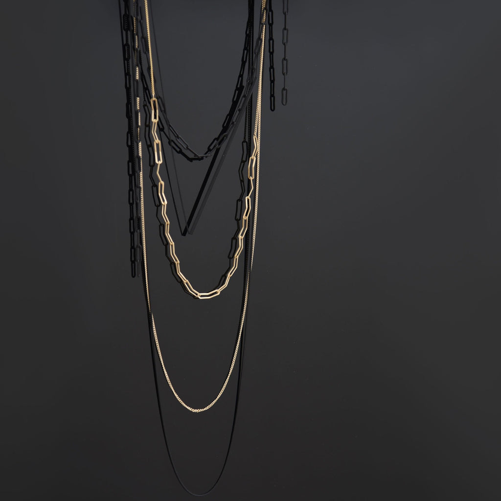 A black and golden necklace in front of a black wall.