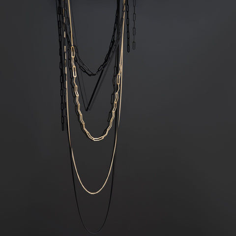 A black and golden necklace in front of a black wall.