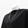 A black and golden necklace on a white mannequin wearing a black shirt.
