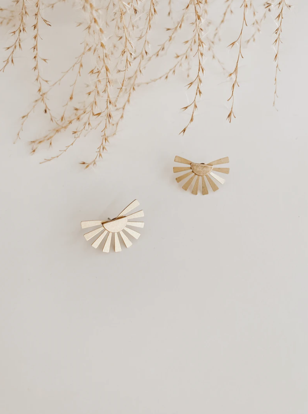 A pair of brass half moon studs in gold lying on a white surface. They are dainty and resemble a sun.