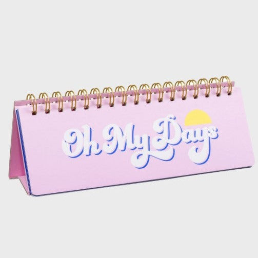 A table calendar in pink with text white and blue letters, saying "Oh my days".