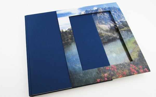 A book with a sleeve showing an idyllic scenery including mountains and a lake. 