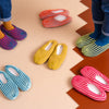 Six pairs of indoor knit slippers with chunky rib stripes in a variety of colorways. 