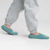 A person with gray sweatpants is wearing indoor knit slippers with chunky rib stripes in teal and light blue.