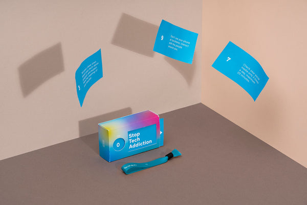 A little blue and pink box with the text: "Stop technology addiction" written on it. Blue cards with text on them are flying around a room, suggesting that they are cards from the box.