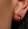Close-up of an ear wearing a golden stud in the form of a heart shape.